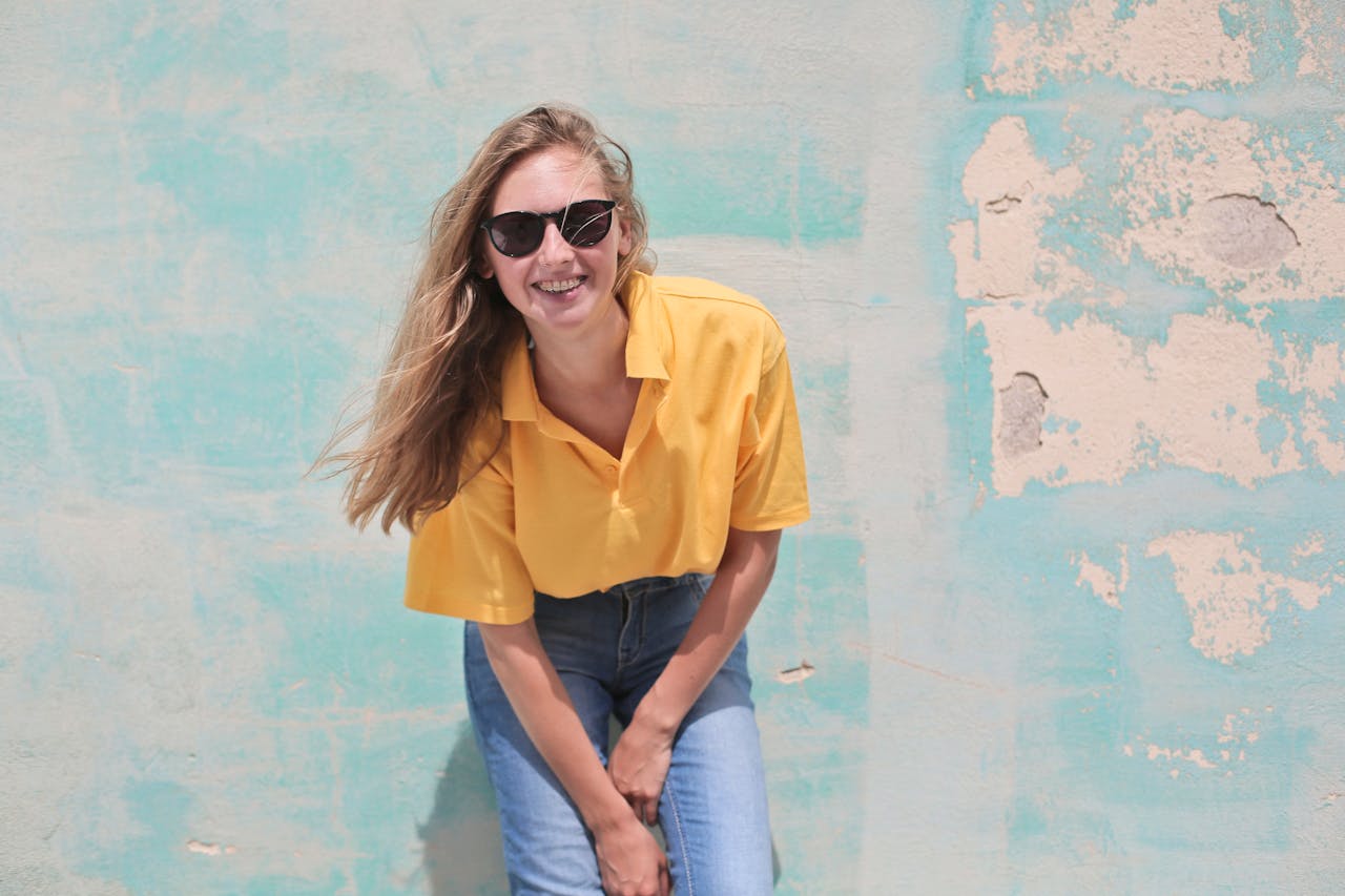 Casual young woman smiling in sunglasses, posing against a vintage colorful wall.