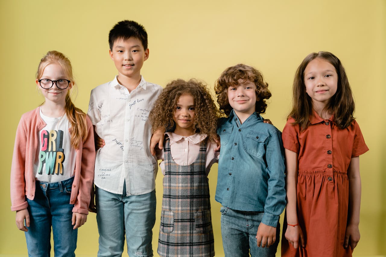 Five diverse children smiling against a yellow background in a studio setting.